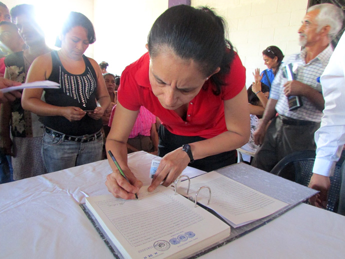 Una de las 199 beneficiarias firma la escritura de propiedad que les brindará seguridad jurídica sobre la propiedad de la tierra que habitan.